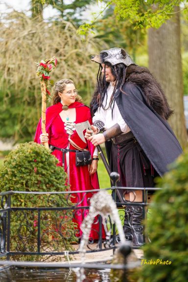 Deux personnages costumés, l'un en rouge avec une canne, l'autre en noir avec une cape.