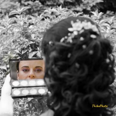 Femme avec une coiffure élégante se regardant dans un miroir, visage partiellement maquillé.
