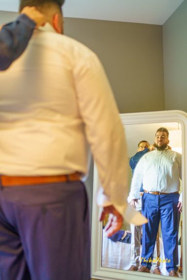 Homme en costume devant un miroir, ajustant sa tenue avec confiance.