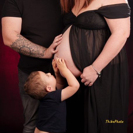Femme enceinte en robe noire, enfant embrassant son ventre, homme à ses côtés.