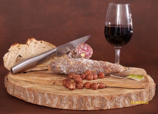 Planche en bois avec charcuterie, noisettes, pain et verre de vin rouge.