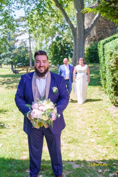 Un homme en costume tient un bouquet, tandis qu'un couple en tenue de mariage s'approche.