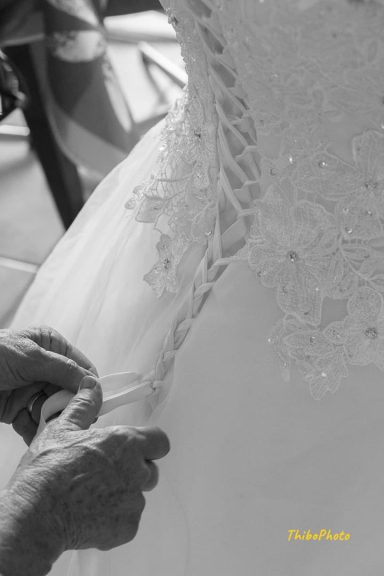 Mains ajustant délicatement la traîne d'une robe de mariée ornée.