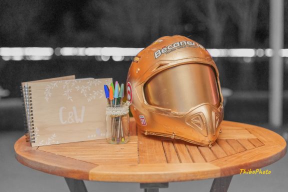 Casque de pilote doré posé sur une table en bois, avec un carnet et des stylos.