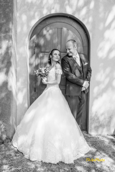 Un couple heureux en tenue de mariage, devant une porte, avec des ombres élégantes.