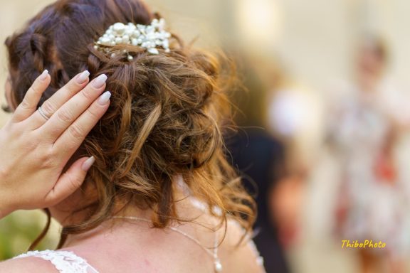 Femme de dos avec un chignon décoré, main sur l'oreille, arrière-plan flou.