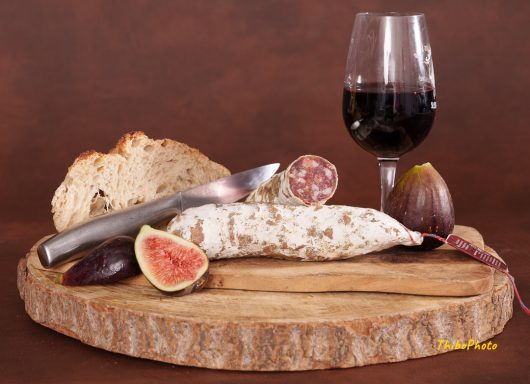 Assiette de charcuterie avec pain, figues et verre de vin rouge sur une planche en bois.