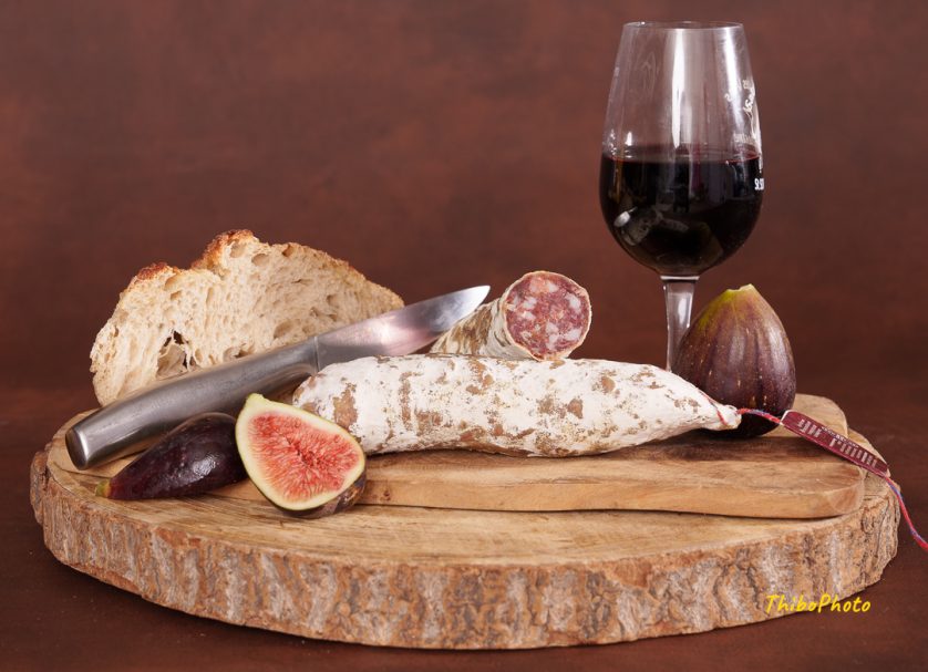 Assiette de charcuterie avec pain, figues et verre de vin rouge sur une planche en bois.