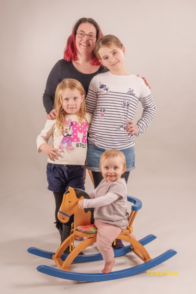 Une femme et trois enfants, dont un bébé sur un cheval à bascule, posent ensemble.