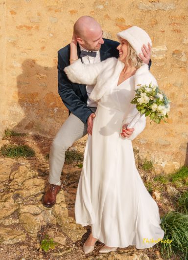 Un couple souriant en tenue de mariage, posant dans un environnement rustique.