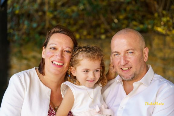 Une femme, un homme et une petite fille sourient ensemble en extérieur.