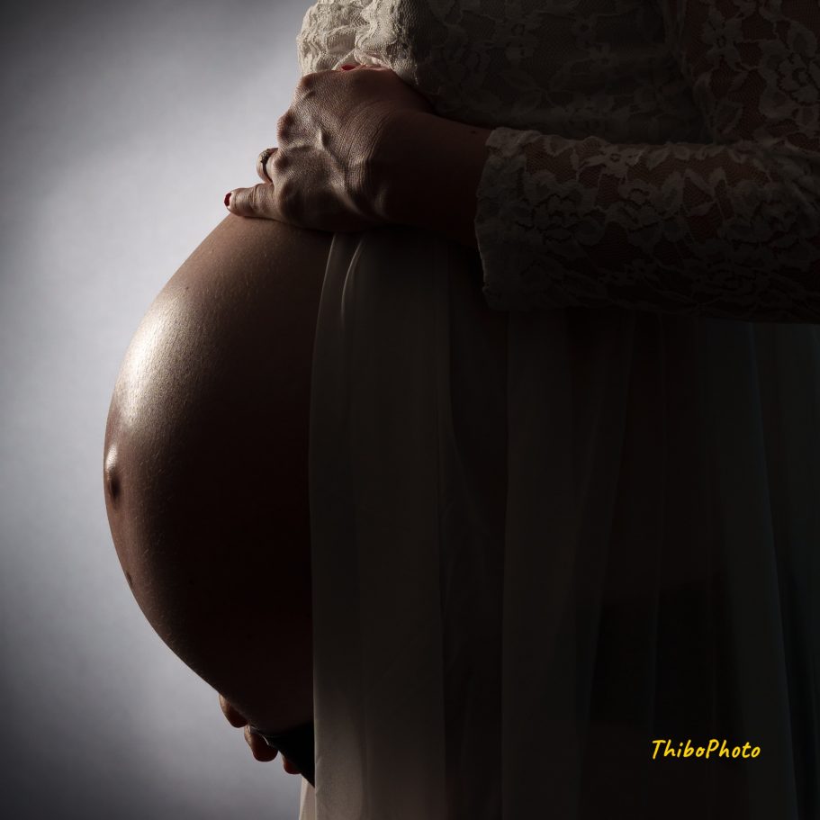 Ventre de femme enceinte éclairé, enveloppé d'une légère robe blanche.