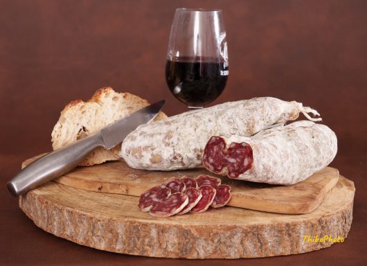 Saucisse sèche, pain, verre de vin rouge et couteau sur une planche en bois.