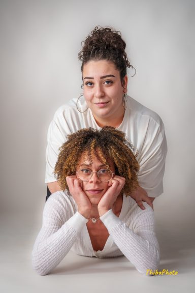 Deux femmes posant ensemble, l'une derrière l'autre, avec des expressions amicales.