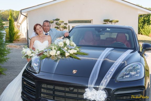 Mariés posant joyeusement devant une voiture Porsche ornée de fleurs.