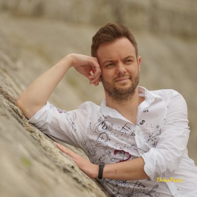 Homme souriant en chemise blanche, reposant sur une surface rocheuse.