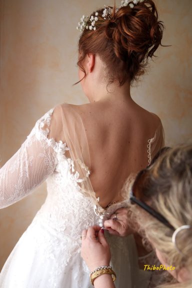 Une mariée ajuste son corsage, vue de dos, avec une coiffe élaborée.