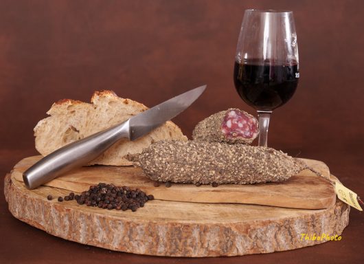 Planche en bois avec un saucisson, du pain, des grains de café et un verre de vin.