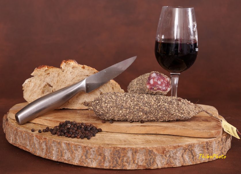 Planche en bois avec un saucisson, du pain, des grains de café et un verre de vin.