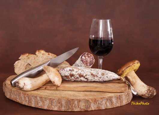 Plateau de charcuterie avec pain, champignons et verre de vin rouge.