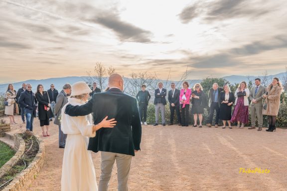 Mariage en plein air avec invités, couple de dos devant un ciel nuageux au crépuscule.