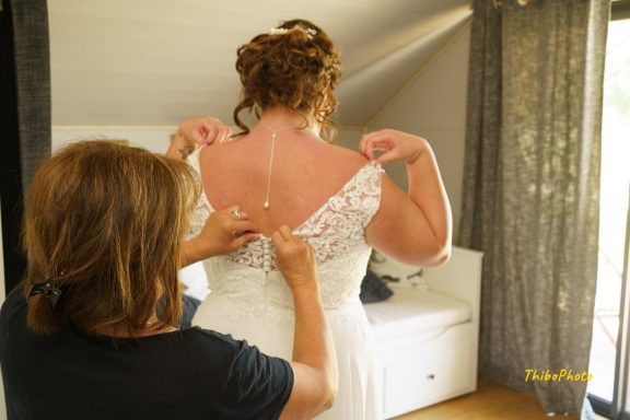 Une femme ajuste la fermeture d'une robe de mariée sur une autre femme.