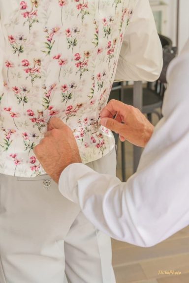 Une personne ajuste le dos d'une chemise à fleurs sur un autre individu.