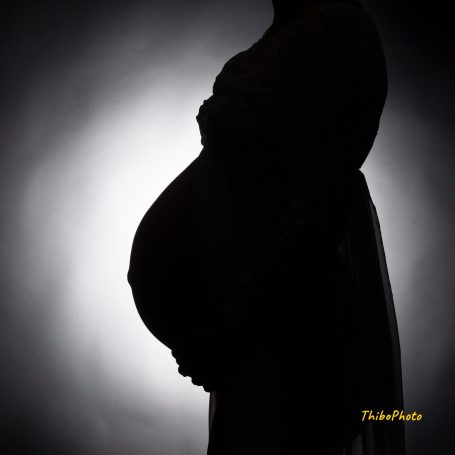 Silhouette d'une femme enceinte, mettant en avant son ventre rond contre un fond lumineux.