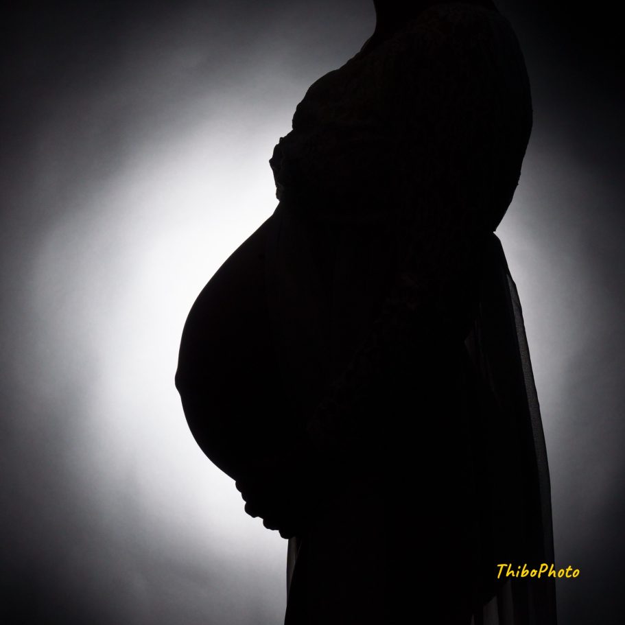Silhouette d'une femme enceinte, mettant en avant son ventre rond contre un fond lumineux.