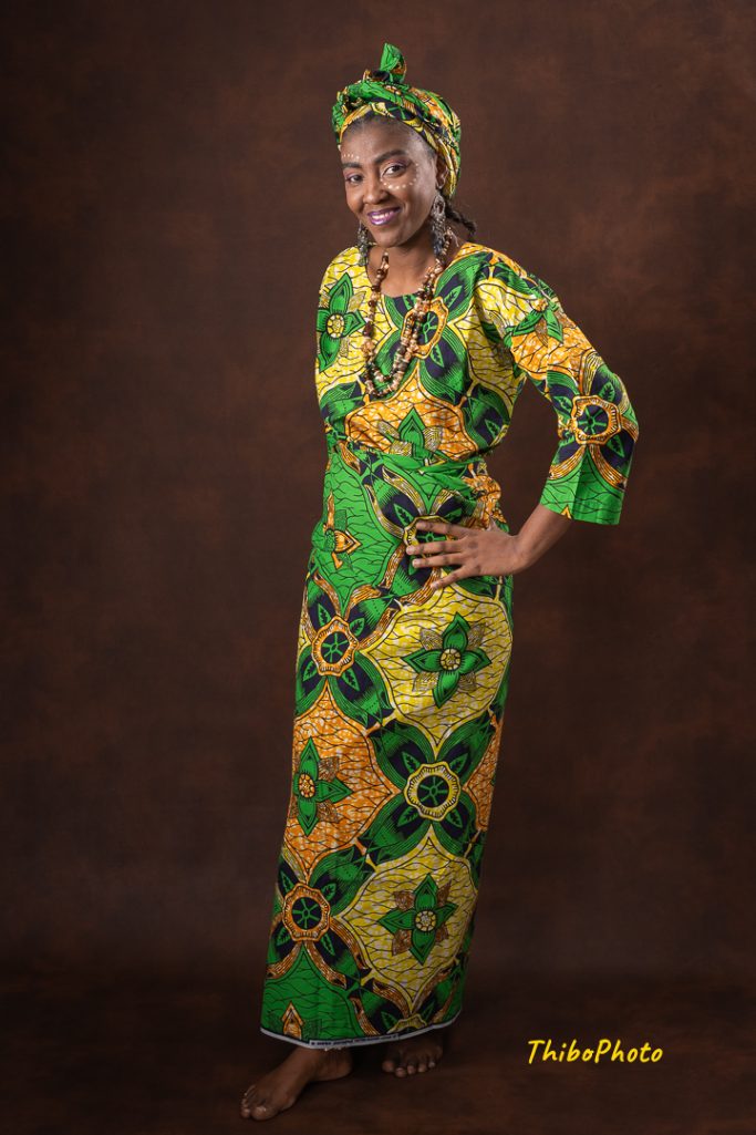 Femme en tenue traditionnelle colorée, posant sur fond marron.