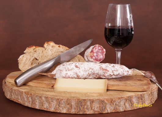 Plateau de charcuterie avec du pain, du fromage, un verre de vin rouge et un couteau.