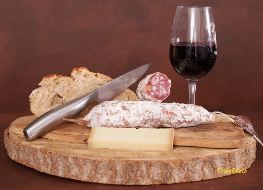Plateau de charcuterie avec du pain, du fromage, un verre de vin rouge et un couteau.