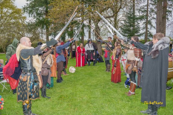 Des participants en costumes médiévaux brandissent des épées lors d'un événement en plein air.