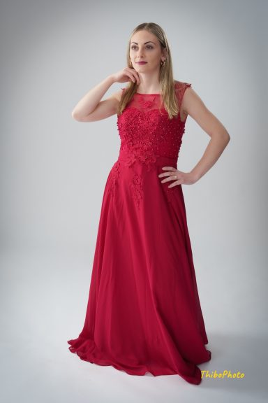 Femme en robe longue rouge posant avec une main sur le cou et l'autre sur la taille.