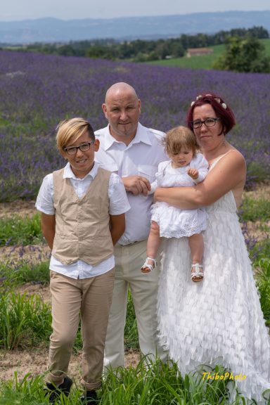 Famille posant dans un champ de lavande, souriant, avec un bébé dans les bras.