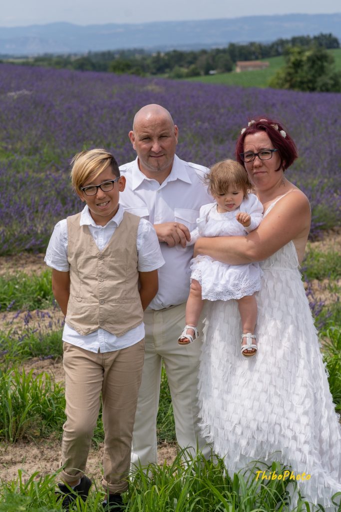 Famille posant dans un champ de lavande, souriant, avec un bébé dans les bras.